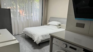 A hotel room with a bed, a washing machine, a TV, and a desk.