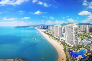Un complejo turístico costero con hoteles frente a la playa, una playa de arena y un mar azul cristalino.