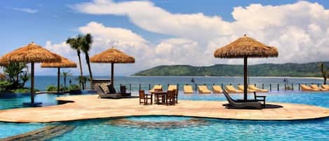A poolside area with lounge chairs and thatched umbrellas, overlooking a body of water.