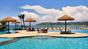 A pool area with lounge chairs and thatched umbrellas, overlooking a beach. - Linghai Seaview Apartment (Huizhou Huidong Shili Yintan Shop) (Huidong)
