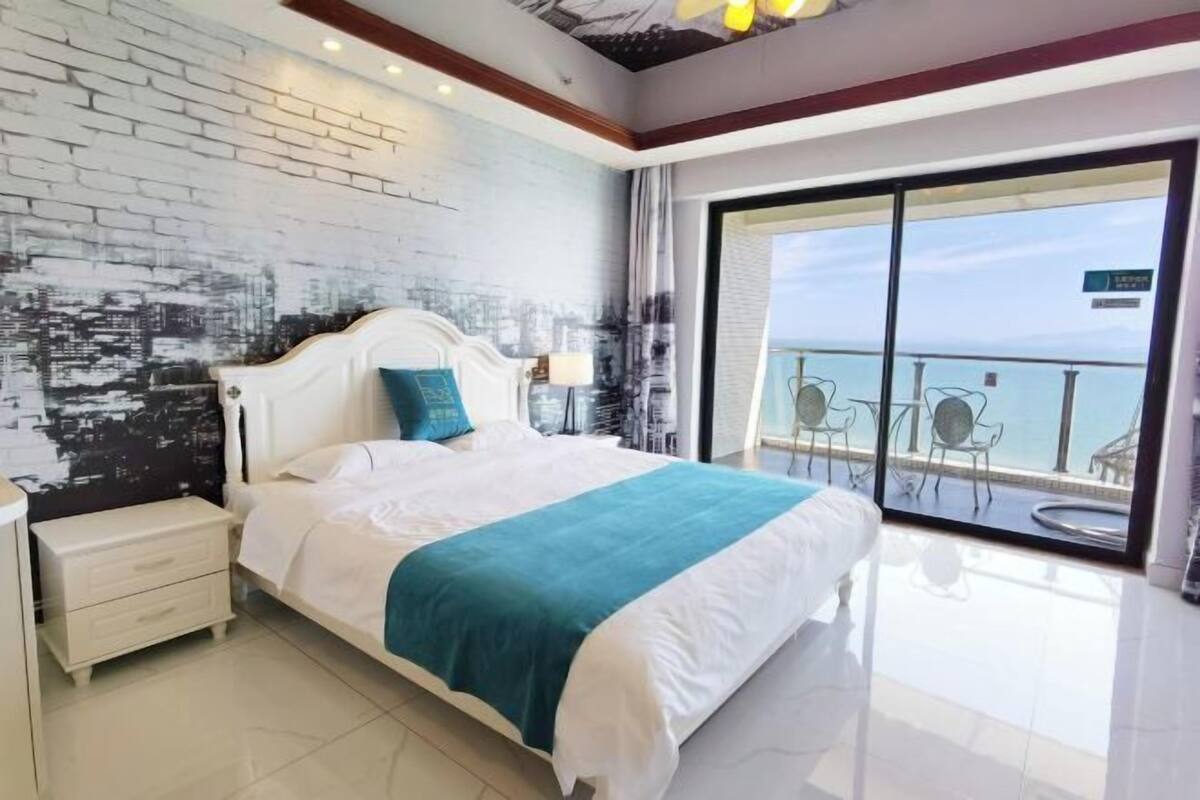 Een hotelkamer met een groot bed, een nachtkastje, uitzicht op zee door een schuifdeur en een moderne bakstenen muur.