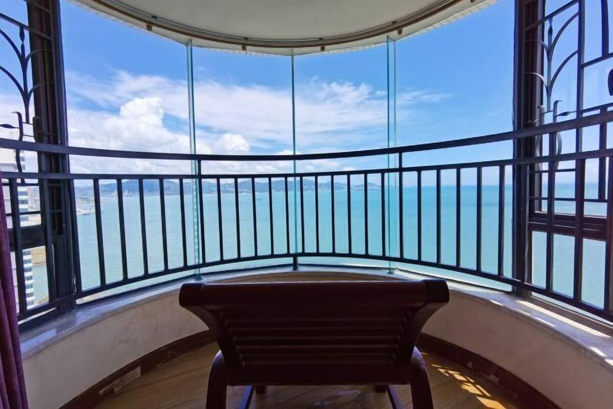 Een balkon op de hoek met uitzicht op zee, een houten bankje en een gebogen plafond.