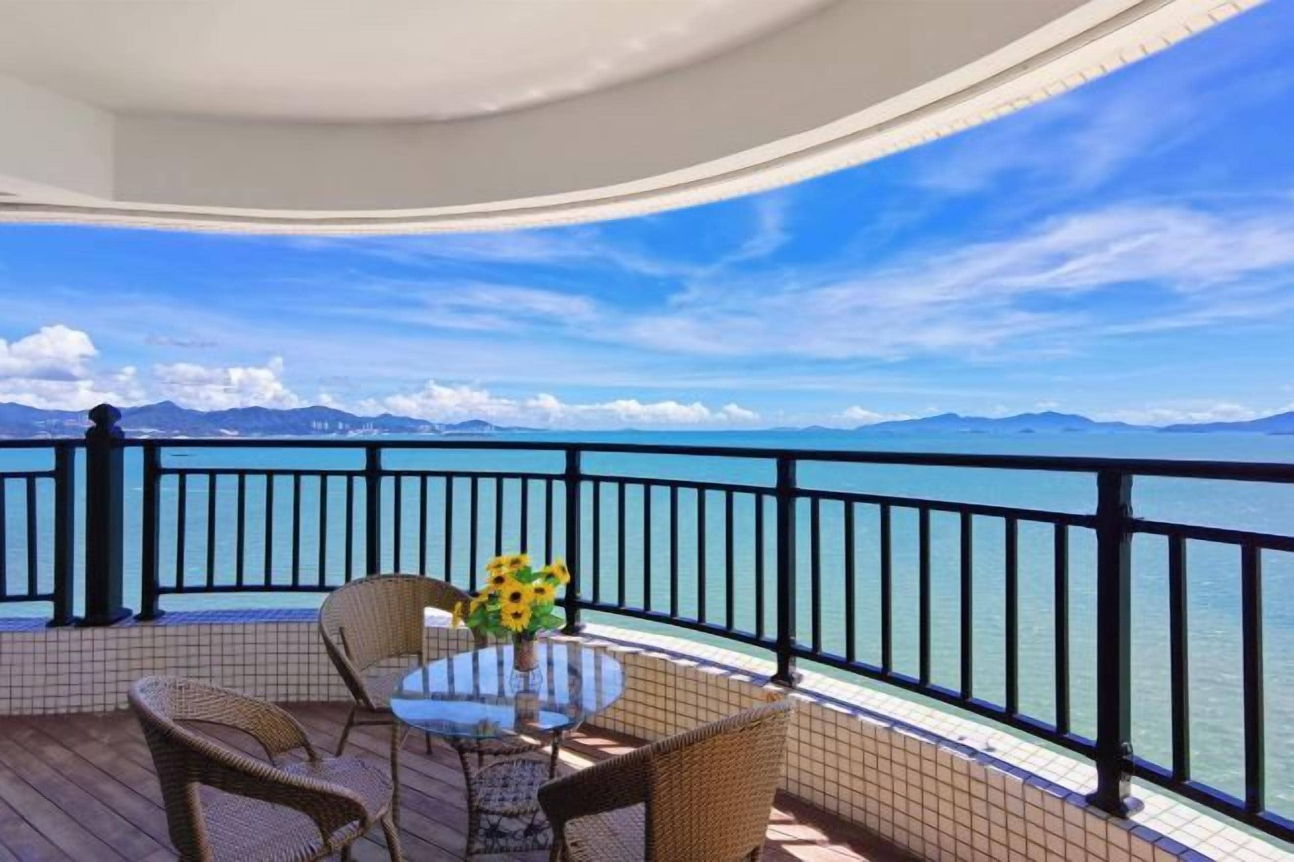 A balcony with a table and chairs, overlooking a body of water and distant mountains.