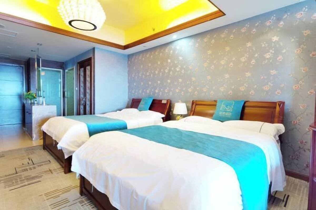 Een hotelkamer met twee bedden, een kroonluchter, bloemenbehang en een houten deur.