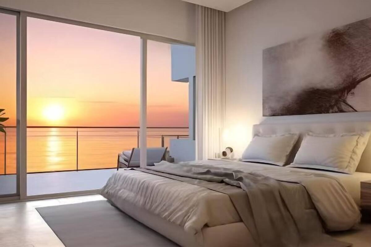 Een moderne slaapkamer met een groot bed, uitzicht op de zonsondergang en een schilderij aan de muur.