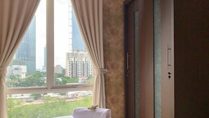 A hotel room with a bed, a window with curtains, a view of tall buildings, and a door with a key lock. - Spacious and Nice 2BR Apartment (Executive City Home unit) at Thamrin Residence (Jakarta)