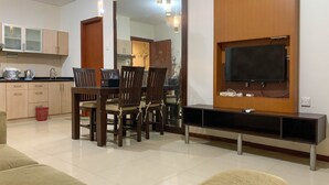 A modern living room with a dining area, a kitchen, and a TV mounted on the wall. - Spacious and Nice 2BR Apartment (Executive City Home unit) at Thamrin Residence (Jakarta)