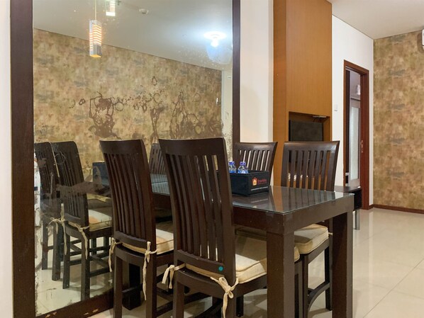 A dining area with a glass table and wooden chairs, a stone wall, and a door.