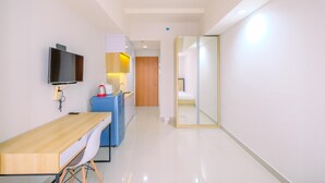 A modern hotel room with a wooden desk, a flat-screen TV, a small kitchenette, and a glass partition separating the bedroom from the living area. - Cozy Stay and Comfort Studio at Evenciio Margonda Apartment (Depok)