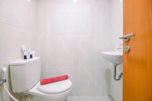 A small, clean bathroom with a toilet, sink, and a wooden door. - Cozy Stay and Comfort Studio at Evenciio Margonda Apartment (Depok)