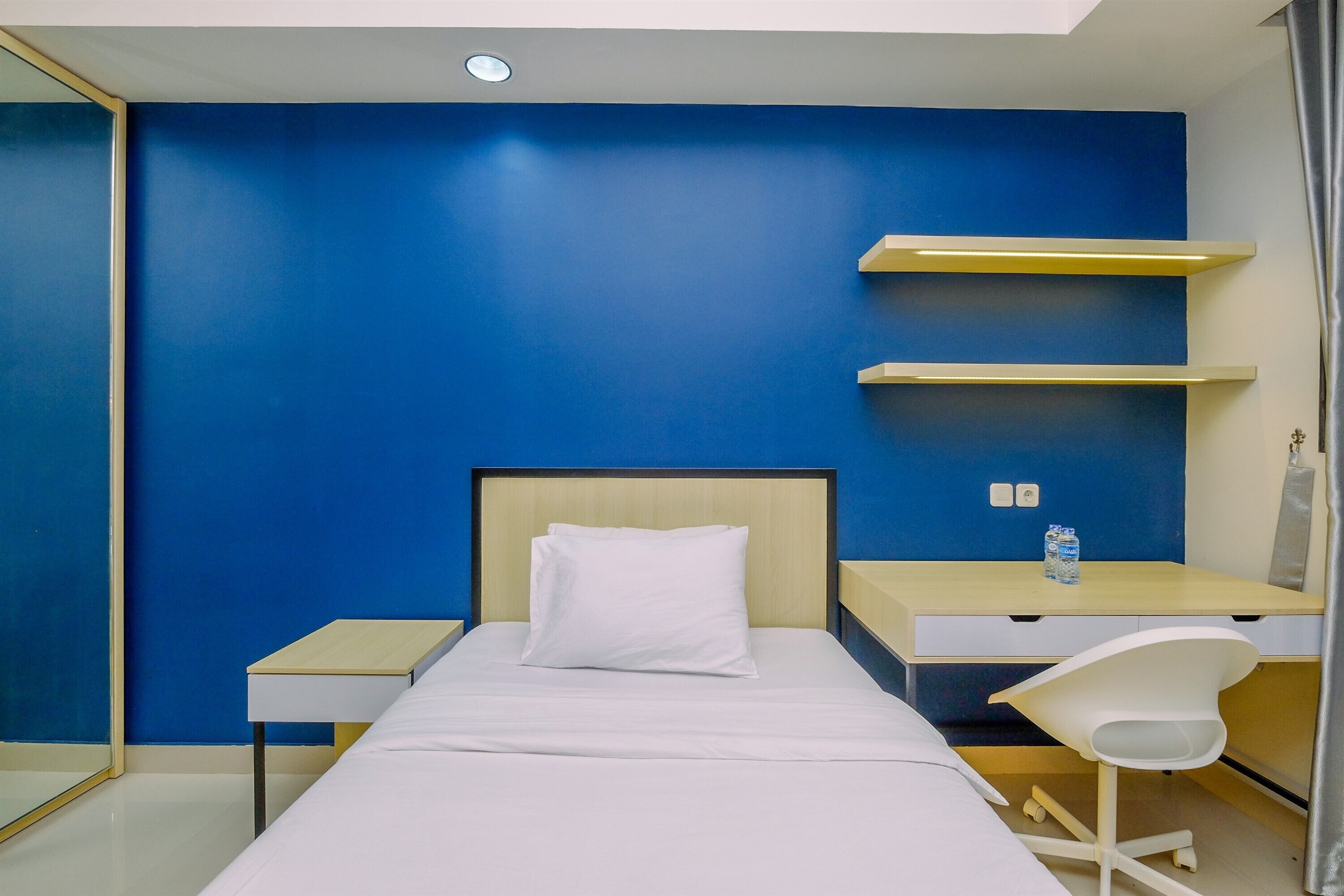 A hotel room with a bed, a desk, a chair, and built-in shelves.