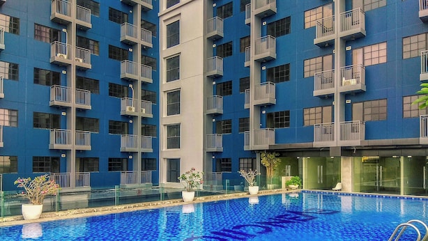 A swimming pool surrounded by a modern building with balconies. - Comfy and Minimalist Studio with City View at Evenciio Margonda Apartment (Depok)