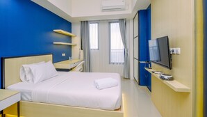 A hotel room with a bed, bedside table, TV, air conditioning unit, and a window with curtains. - Comfy and Minimalist Studio with City View at Evenciio Margonda Apartment (Depok)