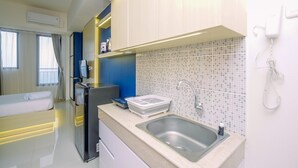 A modern hotel room with a bed, a refrigerator, a sink, and a telephone. - Comfy and Minimalist Studio with City View at Evenciio Margonda Apartment (Depok)