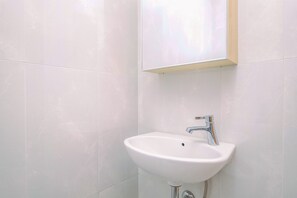 Casa de banho com azulejos brancos, lavatório branco e torneira cromada.