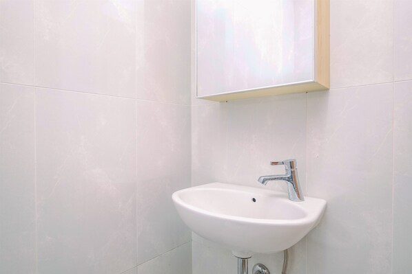 A bathroom with white tiles, a white sink, and a chrome faucet. - Comfy and Minimalist Studio with City View at Evenciio Margonda Apartment (Depok)