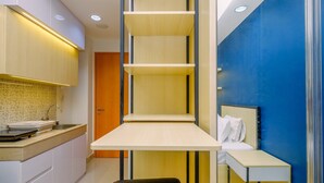 A compact hotel room with a kitchenette, a bed with a headboard, and a small desk. - Comfy and Minimalist Studio with City View at Evenciio Margonda Apartment (Depok)