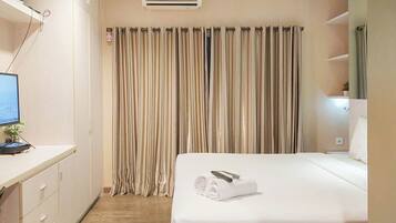 A hotel room with a bed, a desk with a computer, and a curtain.
