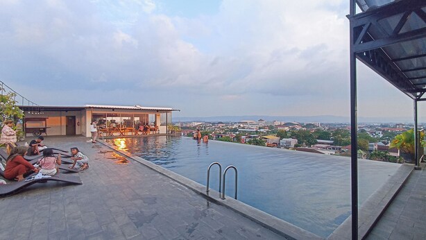 A rooftop infinity pool with a city view, lounge chairs, and a bar area. - Good and Homey Studio at Student Park Yogyakarta Apartment (Depok)