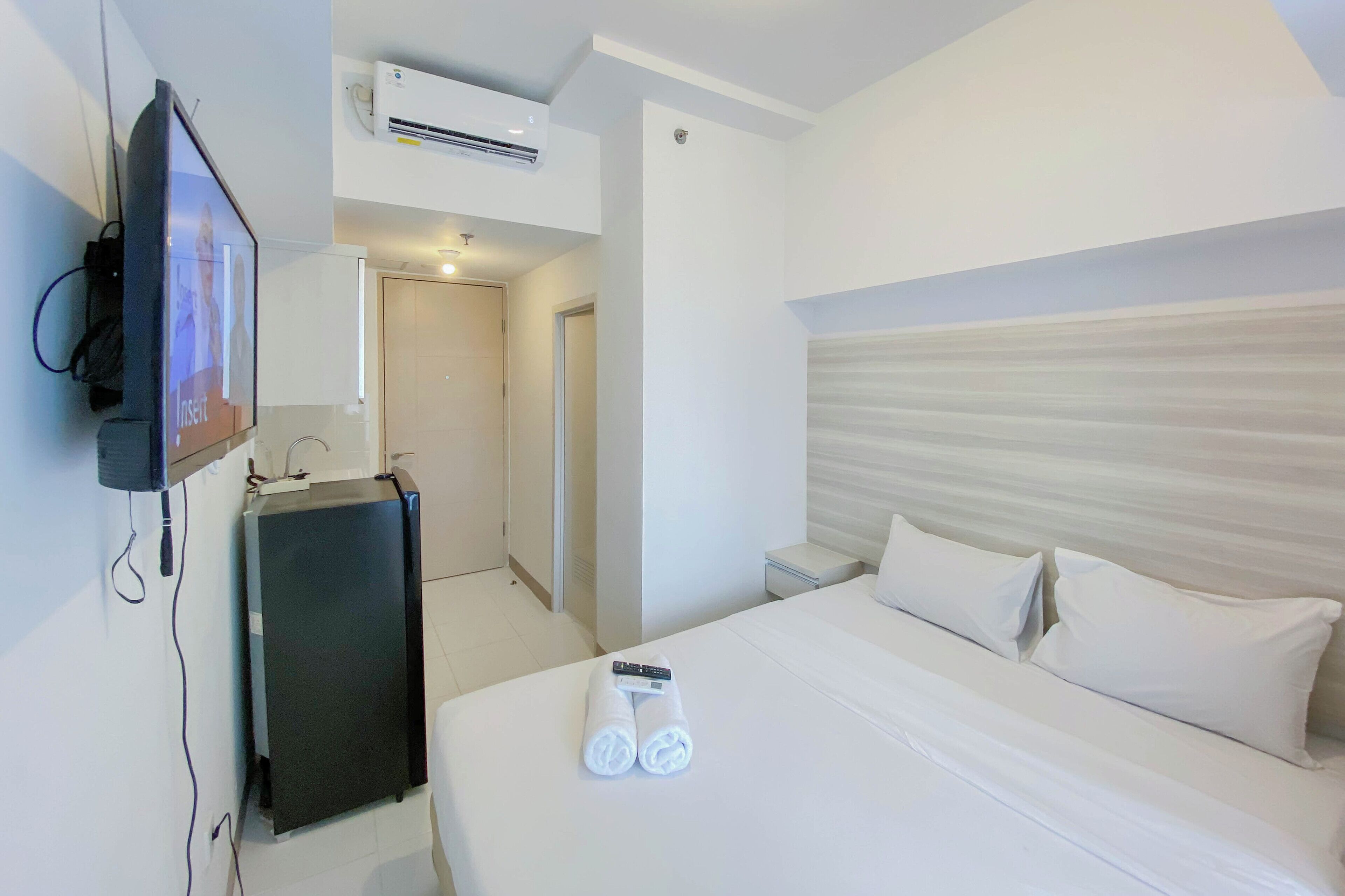 A hotel room with a bed, a TV mounted on the wall, a desk, and a minibar.