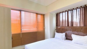 Une chambre à coucher avec un grand lit, des stores en bois, une tête de lit agrémentée de rideaux et une fenêtre également équipée de stores.