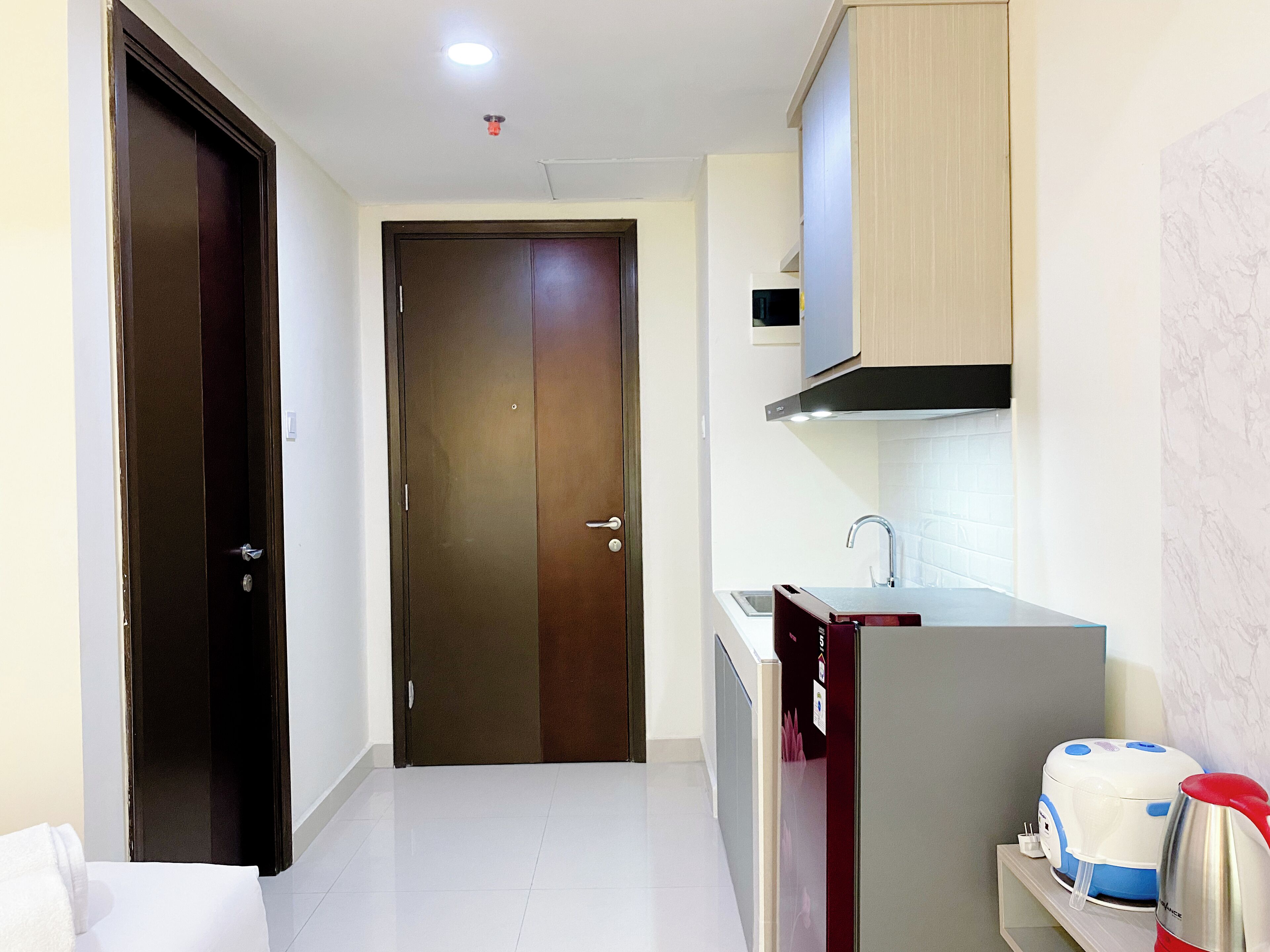 A narrow hallway with a closed door, a kitchenette with a sink, and a microwave.