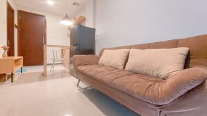 A modern living room with a beige sofa, a wooden side table, a small dining table, and a TV.