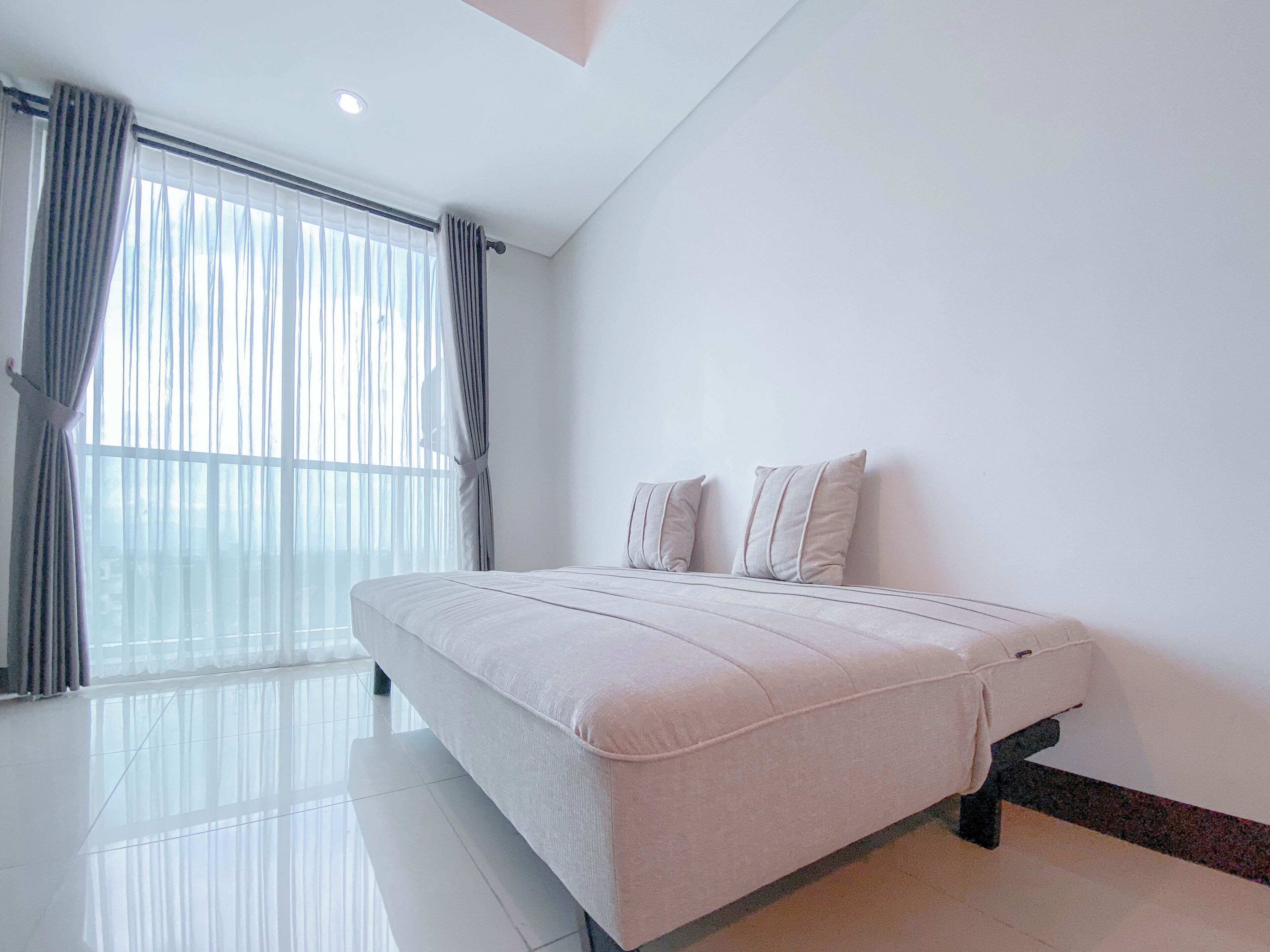 Een moderne slaapkamer met een groot bed, witte wanden en een ruim raam met gordijnen.
