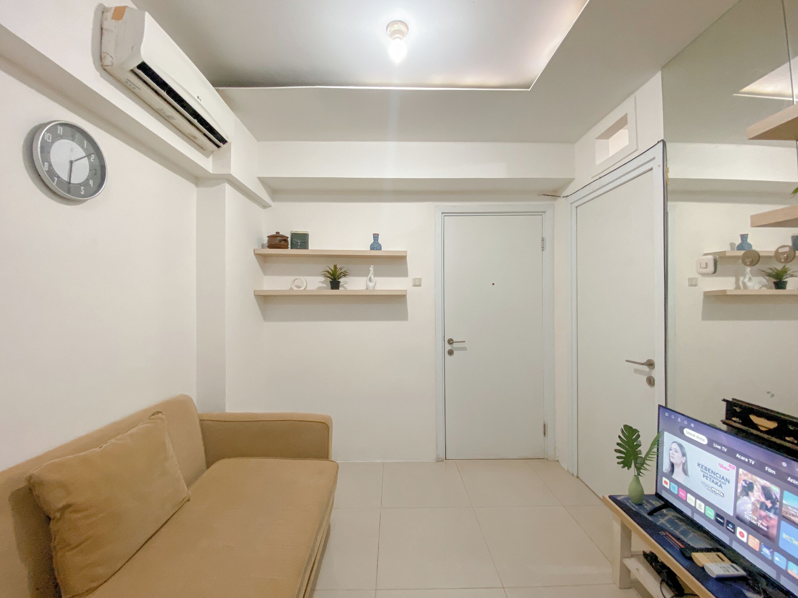 A living room with a beige sofa, a flat-screen TV, and a ceiling light.
