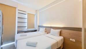 Une chambre d’hôtel avec deux lits, une grande fenêtre avec des stores, une tête de lit en bois et une table de chevet.