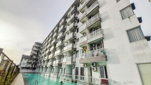 Un immeuble résidentiel à plusieurs étages, doté de balcons, d’une piscine et de climatiseurs.