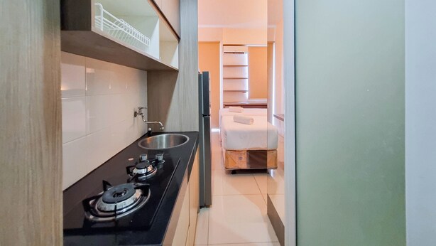 Une cuisine compacte équipée d’une cuisinière à gaz et d’un petit évier, donnant sur une chambre avec un lit et une armoire.