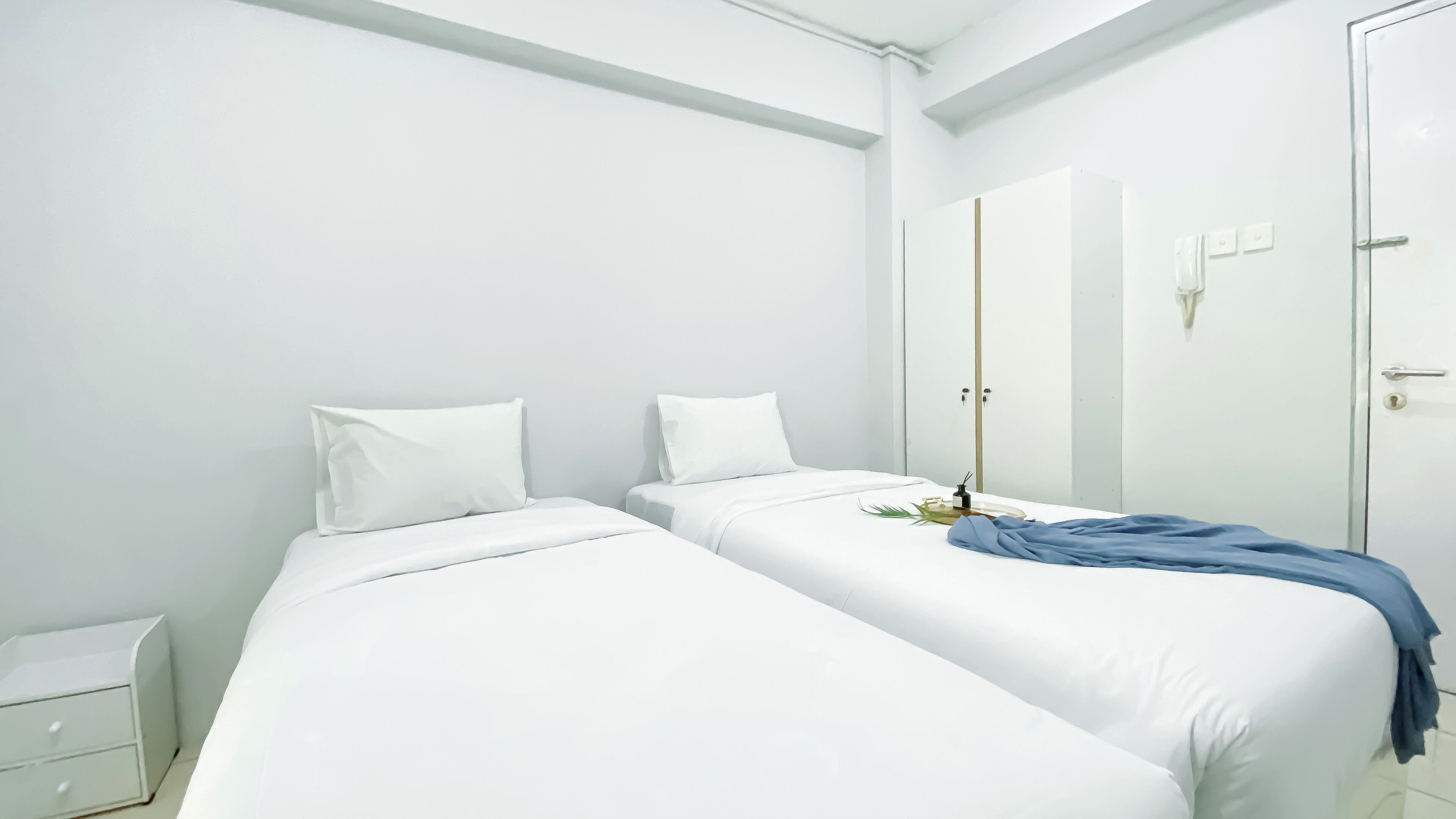 A minimalist bedroom with two beds, a wardrobe, and a bedside table.