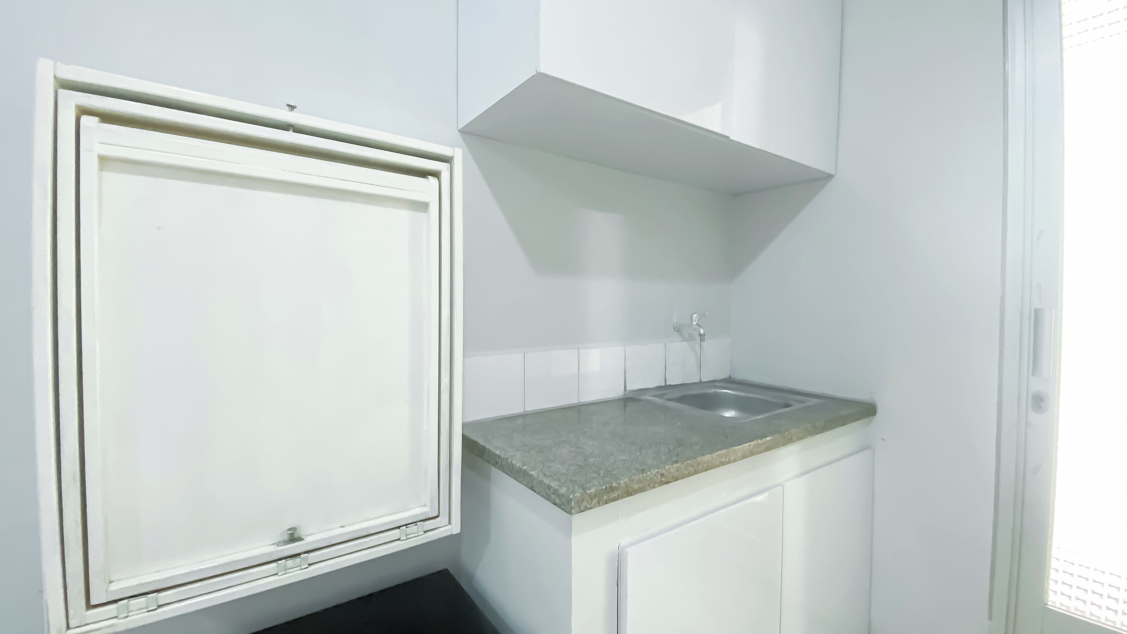 Une petite cuisine blanche, avec un seul évier et une fenêtre au-dessus.