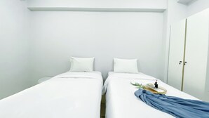 A room with two single beds, white walls, and a door.
