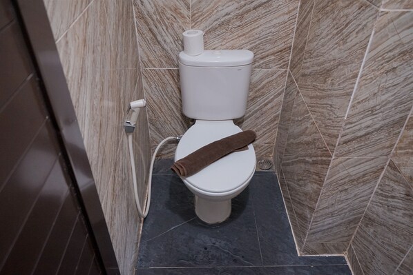 A toilet with a towel on the seat, a toilet paper holder, and a marble-patterned wall. - Luxurious 2BR at Urbantown Serpong Apartment (South Tangerang)