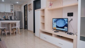 Una cucina moderna con frigorifero integrato, un'area pranzo con tavolo e sedie bianche e una TV su un supporto in legno.