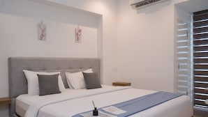Un letto rifatto con cura, con testiera grigia, cuscini bianchi e grigi e una coperta azzurra. Sopra il letto, due opere d'arte appese alla parete, e un comodino di legno accanto.