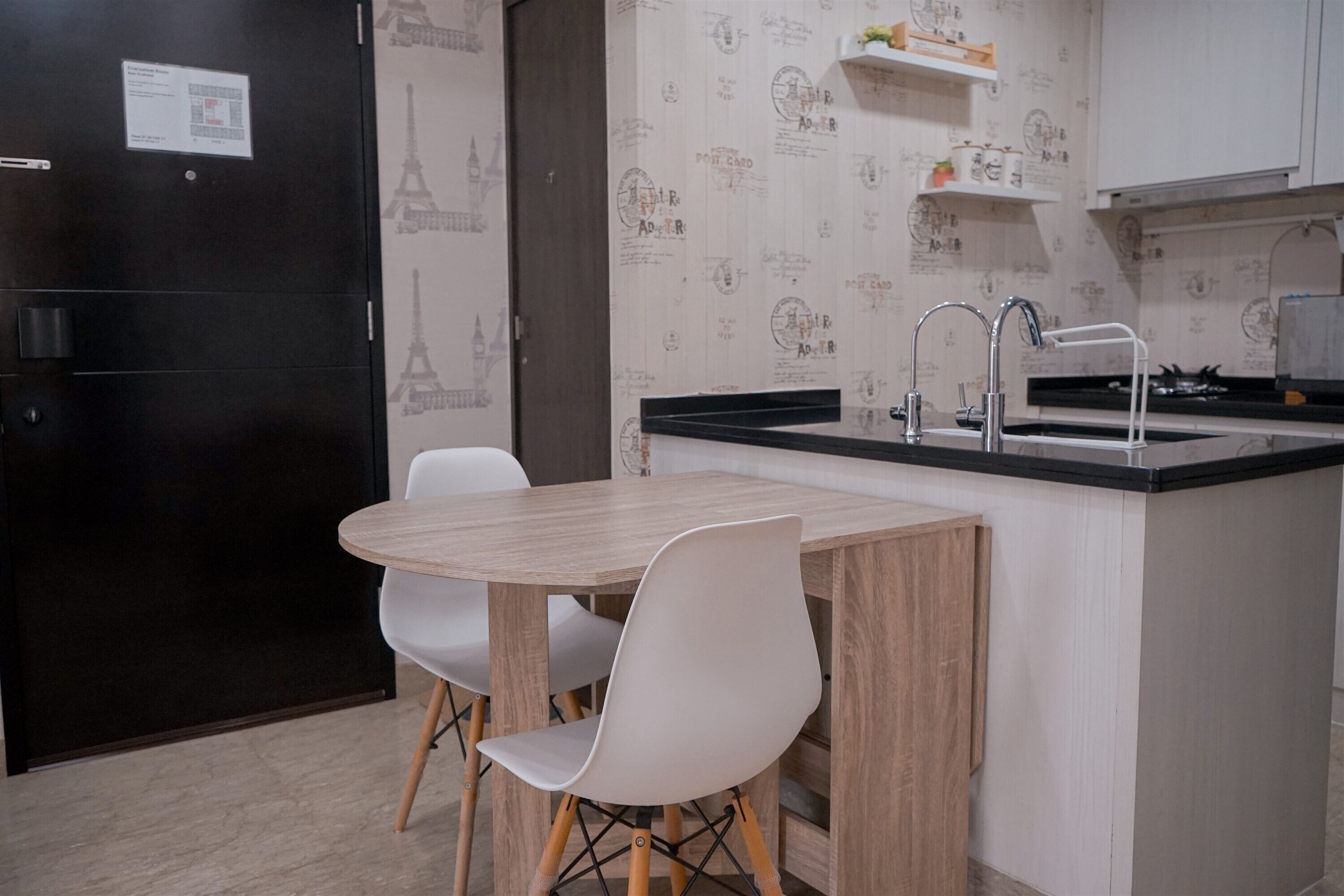 Una cocina compacta con una mesa de madera y sillas blancas, un refrigerador negro y un lavamanos con grifo.