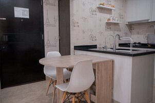 A compact kitchen with a wooden table and white chairs, a black refrigerator, and a sink with a faucet.