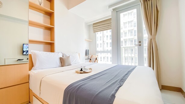 A hotel room with a bed, a desk, and a window with curtains. - Nice Room Studio Apartment at Tokyo Riverside PIK 2 (Teluknaga)