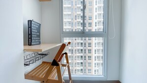 A corner room with a window overlooking a residential building, a wooden chair, and a blackboard listing travel destinations. - Nice Room Studio Apartment at Tokyo Riverside PIK 2 (Teluknaga)