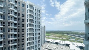 A high-rise building with multiple balconies and a view of a coastal area with greenery and a road. - Nice Room Studio Apartment at Tokyo Riverside PIK 2 (Teluknaga)