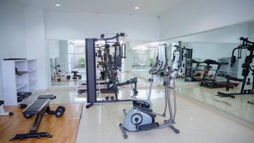 Un gimnasio con diversos equipos de ejercicio, un espejo grande en la pared y suelo de madera.