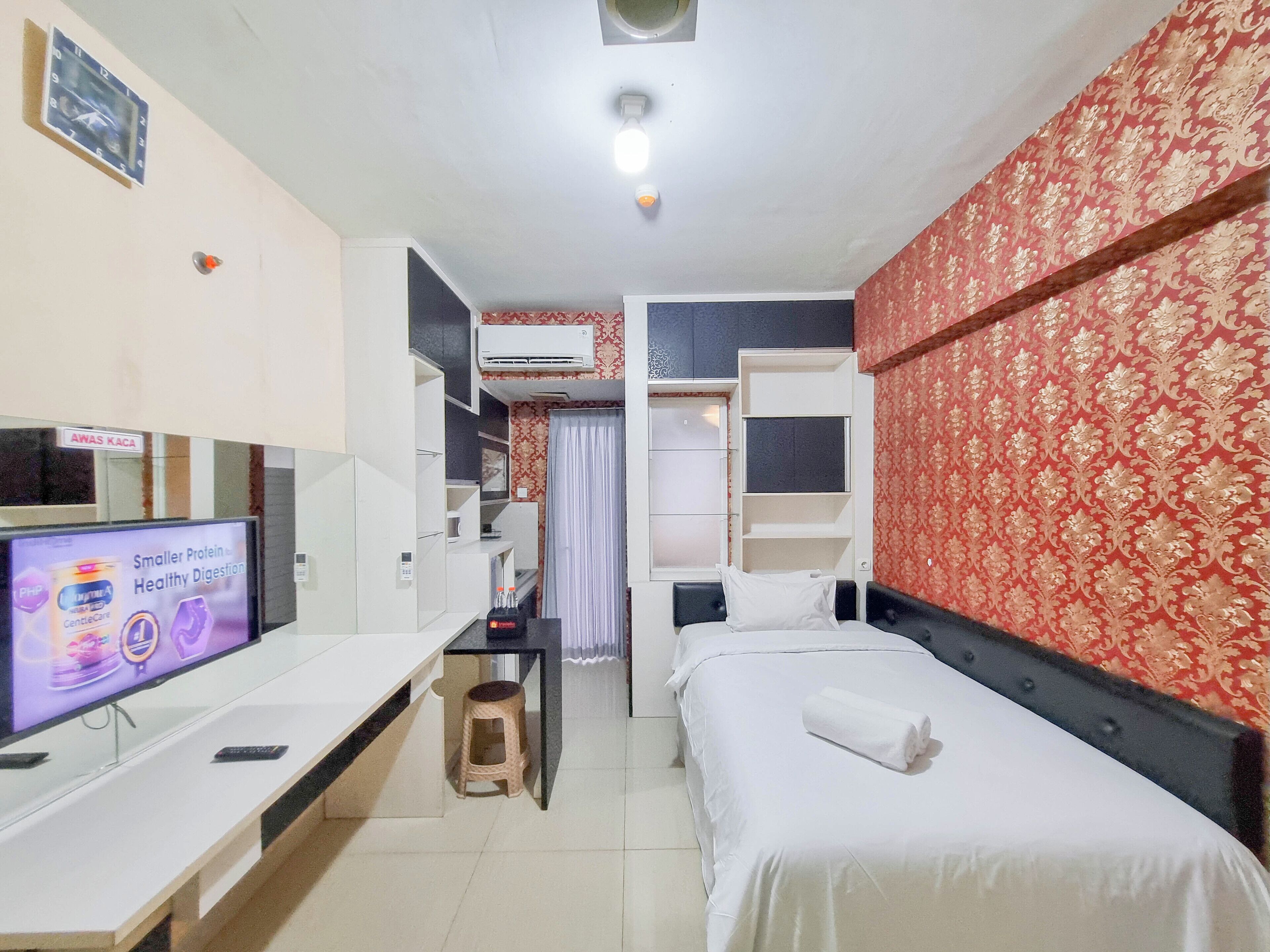 Habitación de hotel con cama, escritorio con televisor, armario y baño visible a través de una puerta abierta.