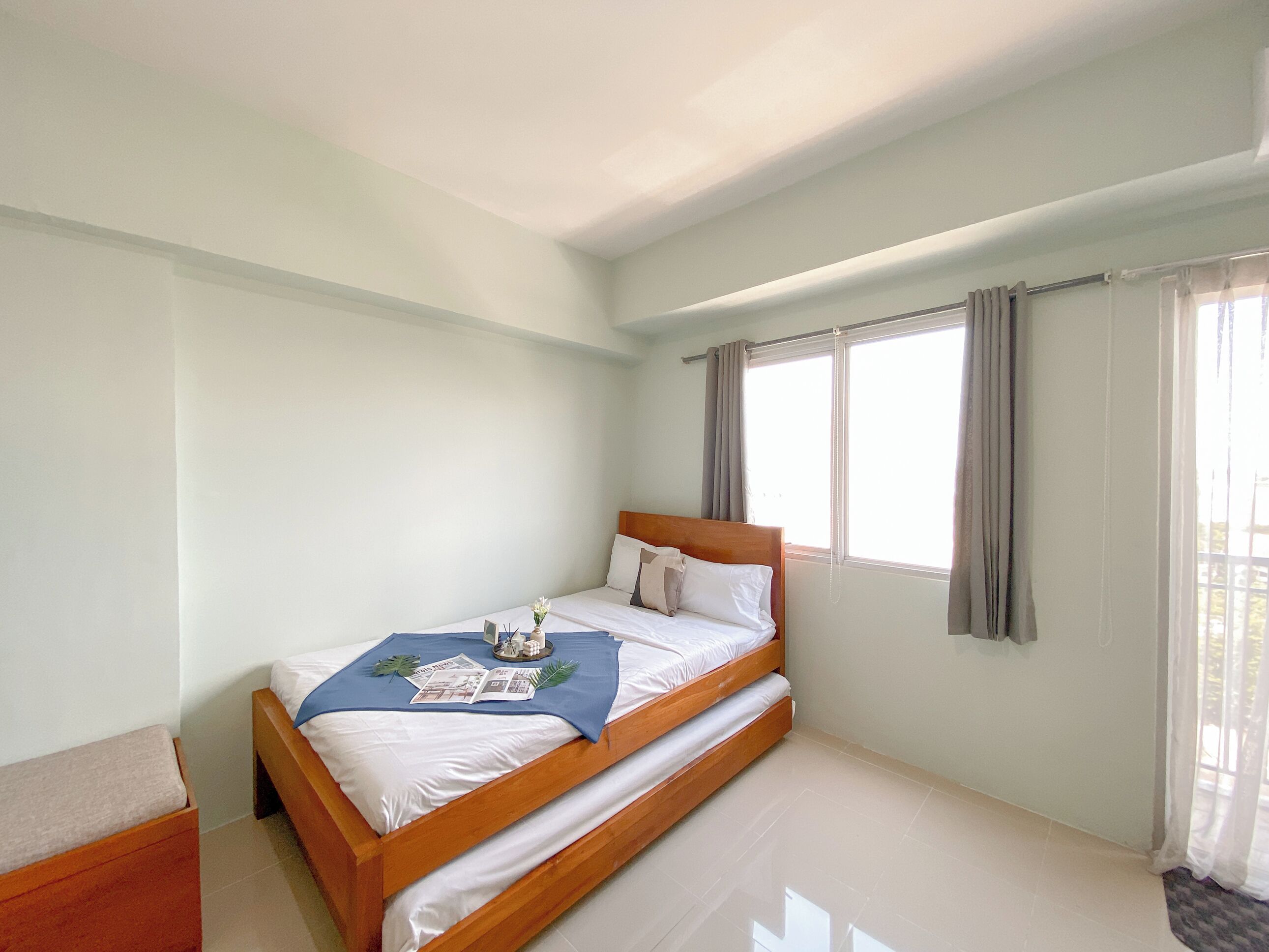 A single-bed room with a wooden headboard, a bedside table, and a window with curtains.