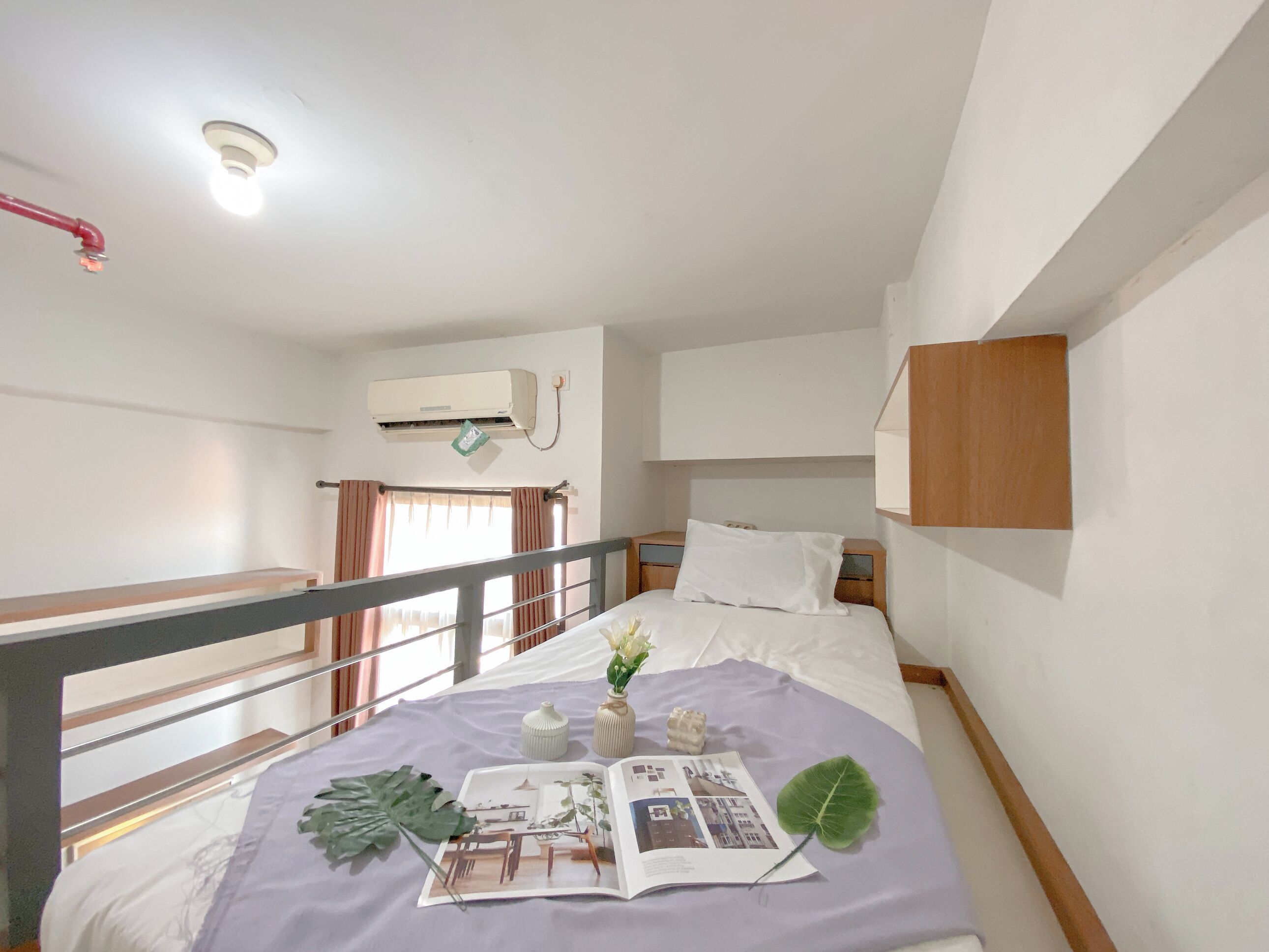 Un dormitorio con cama, mesita de noche, ventana con cortinas, equipo de aire acondicionado y una pequeña estantería de madera.