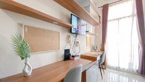 Un espace de bureau moderne comprenant un bureau en bois, un tableau d’affichage en liège, un téléviseur à écran plat et un téléphone.