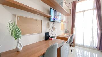 A modern office space with a wooden desk, a corkboard, a flat-screen TV, and a telephone.