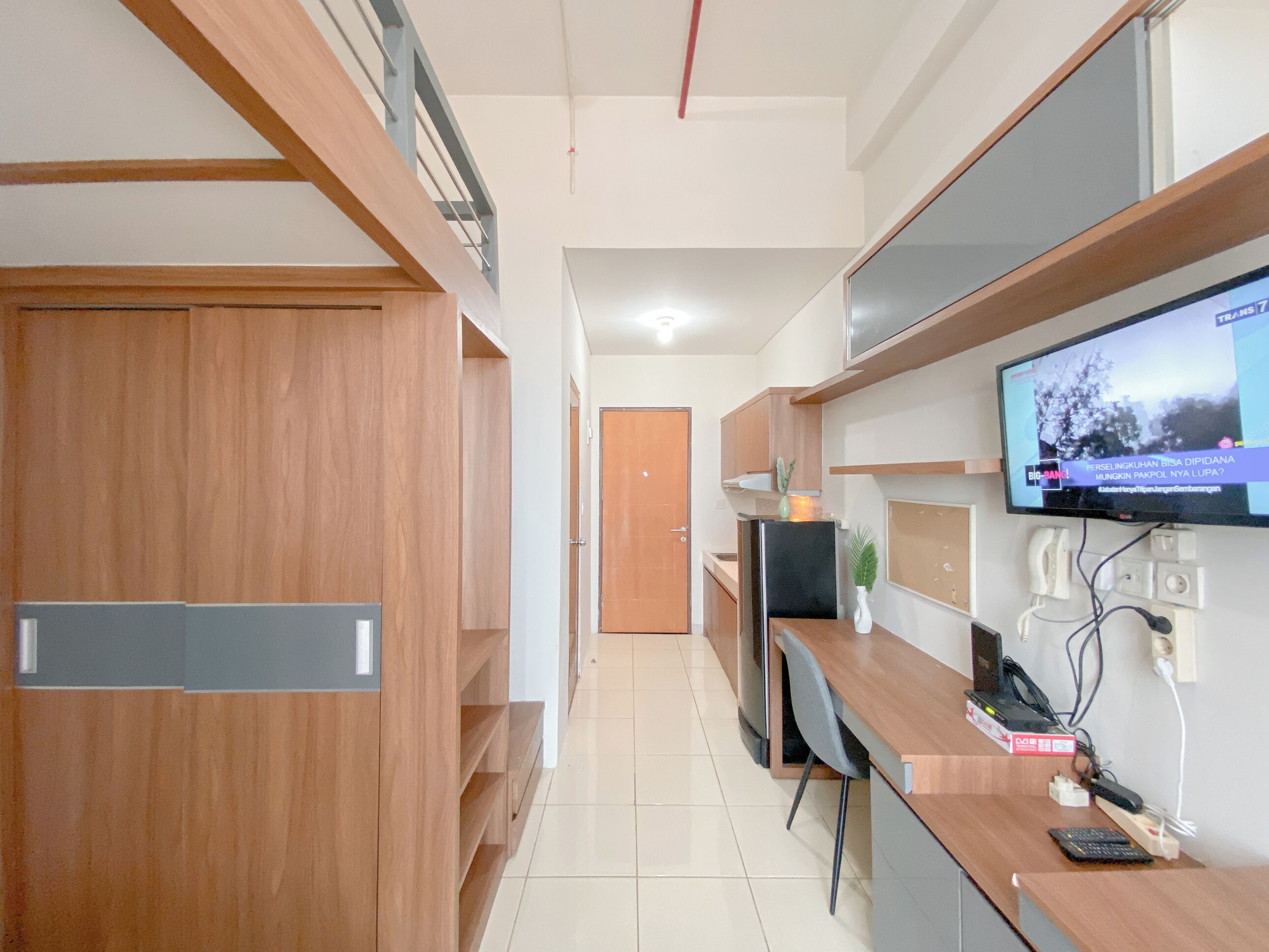 A modern kitchen with wooden cabinets, a built-in oven, and a flat-screen TV mounted on the wall.